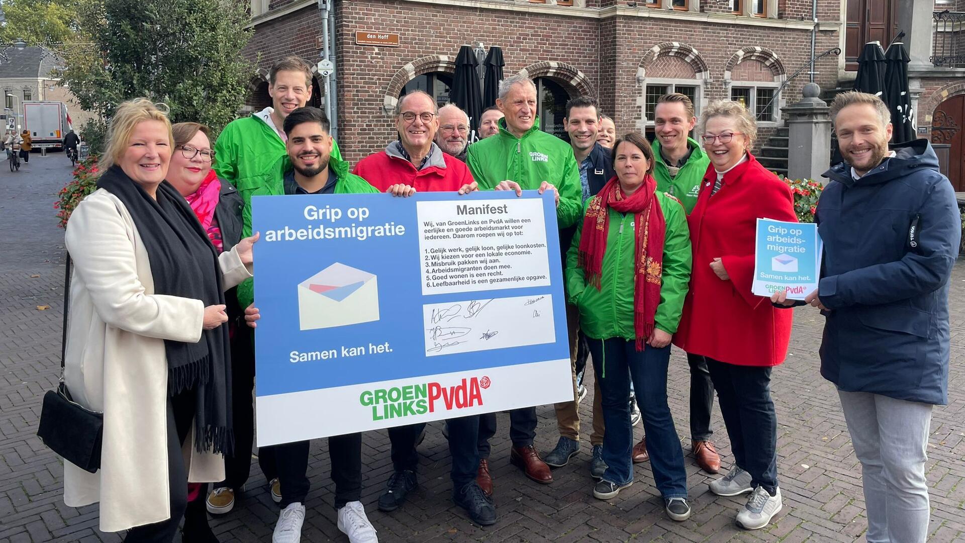 Mariette Patijn samen met een groep mensen in rode en groene jassen met een groot bord waar handtekeningen op staan